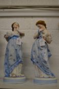 A pair of Continental bisque porcelain figures of standing females holding doves.