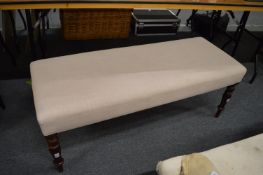 A long upholstered stool on turned legs.