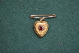 A yellow metal heart shaped pendant set with a single garnet.