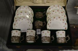 A cased coffee set containing four porcelain cups, six saucers and six silver cup holders.