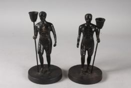 A PAIR OF BRONZE NUBIAN FIGURAL CANDLESTICKS on circular bases. 8ins high.