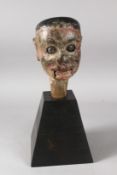 A CARVED AND PAINTED WOODEN MARIONETTE HEAD on a wooden stand. 6ins high.
