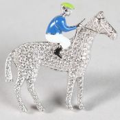 A SILVER AND ENAMEL JOCKEY ON HORSE BROOCH.