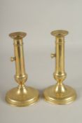 A PAIR OF CIRCULAR BRASS CANDLESTICKS WITH PUSHERS. 21cms high.