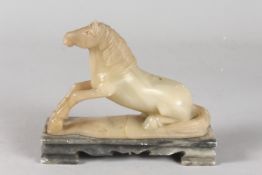 A CHINESE QING DYNASTY GREEN SOAPSTONE CARVING OF A RECUMBENT HORSE, mounted to a rectangular