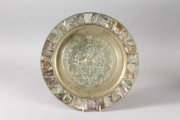 A HIGHLY DECORATIVE EMBOSSED AND ABALONE-INLAID BRASS DISH, with central roundel of archaic style