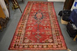 An old Persian rug, red ground with stylised decoration including animals and figures, 290cm x