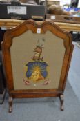 Walnut fire screen, the panel embroidered with an heraldic device.