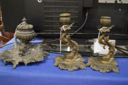 An ornate brass desk set comprising inkwell and pair of candlesticks with stylised dolphin shaped