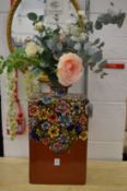 A large floral decorated pottery vase with artificial flowers.