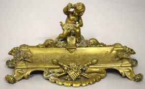 A GOOD BRASS PEN TRAY with cupid and trophies, on four curving feet. 9ins long.