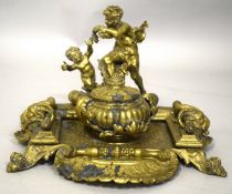 A VERY GOOD BRASS TABLE-DESK INKSTAND with two cupid rams masks and curving feet. 9.5ins long.