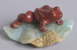 AN EARLY 20TH CENTURY CHINESE CARVED RED AGATE FROG ON A GREEN QUARTZ LILY PAD, 7cm wide.