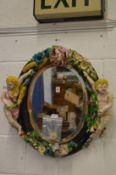 A Majolica style oval pottery wall mirror with cherub and flower decoration.