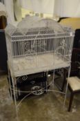 A large white painted wrought iron bird cage with stand.