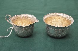 A silver cream jug with embossed decoration and a similar sugar bowl.