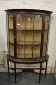 A mahogany bow front display cabinet on stand.