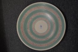 A Poole pottery dish painted with pale green bands and twined pattern of red and blue stripes.