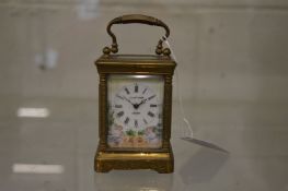 A small brass carriage clock with porcelain dial and panels.