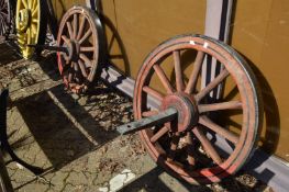 A pair of red painted wooden wagon wheels with iron shafts.
