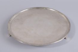 A GEORGE III CIRCULAR SILVER SALVER with bead edge, on three curving feet, shield crest. 13ins
