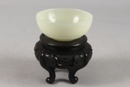 A CHINESE JADE BOWL ON HARDWOOD STAND, bowl 10cm diameter.