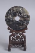 A CHINESE CARVED HARDSTONE BI DISK ON WOODEN STAND, the disk with three chilong, 9.5cm diameter.