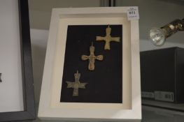 A group of three small bronze crucifixes, mounted and framed.