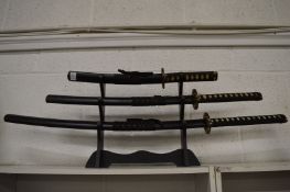 A set of three Japanese swords on stand.