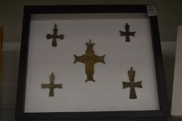 A group of five bronze crucifixes, mounted on a backing board and framed.