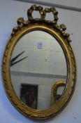 A pair of oval gilt framed mirrors with ribbon and bow cresting.