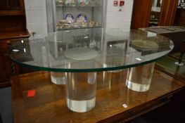 A heavy oval glass coffee table with four cylindrical perspex supports.