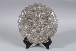 A SMALL EGYPTIAN SILVER OVAL MIRROR with repousse and scroll decoration. 8ins diameter.