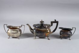 A SILVER TEAPOT on four legs, Sheffield 1912, including the handle, milk jug and sugar basin. Weight