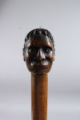 A RARE 19TH CENTURY MAORI WALKING CANE, the handle carved as a Maori head. 36ins long.