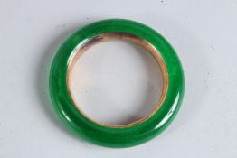AN APPLE GREEN JADE AND GILT METAL BANGLE. 3.5ins diameter.