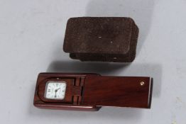 A VAN CLEEF & ARPELS MINIATURE WOODEN CLOCK with sliding top. 2ins x 1ins, in a cloth case.