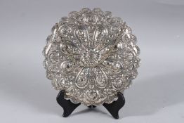 A SMALL EGYPTIAN SILVER OVAL MIRROR with repousse and scroll decoration. 8ins diameter.