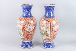 A LARGE PAIR OF IMARI VASES, red and blue with panels of figures and motifs. 24ins high.