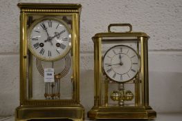A brass four glass clock together with a similar clock.