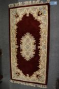 A small Chinese burgundy and floral decorated rug, 150cm x 78cm.
