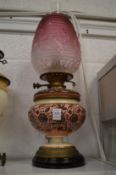A pottery oil lamp converted to electricity with ornate pink tinted glass shade.