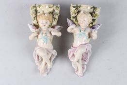 A PAIR OF BISQUE CUPID WALL VASES. 9ins high.