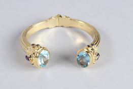 A STERLING SILVER GILT, BLUE TOPAZ, AMETHYST AND SAPPHIRE TORQUE STYLE BANGLE.
