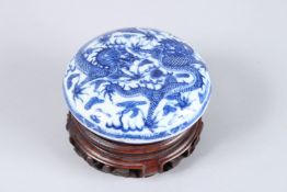 A GOOD SMALL BLUE AND WHITE CIRCULAR BOX AND COVER, on a wooden stand. 3.25ins diameter. Kang-Hi
