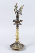AN 18TH CENTURY BRASS OIL LAMP with a bird god, on a circular base. 17ins high.