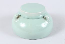 A CHINESE CELADON GLAZED PORCELAIN BOWL AND COVER, with three loop handles. 15cms diameter.