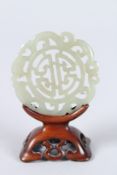 A SMALL PIERCED JADE CIRCULAR TABLET. 2ins diameter, on a wooden stand.