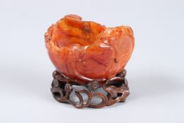 A CHINESE CARVED BOAT SHAPED AGATE BRUSH POT, carved with lilies. 4ins x 2.5ins on a wooden stand.