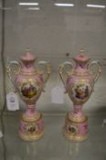 A pair of pale pink ground porcelain twin handled urns, covers and pedestal bases, painted with
